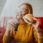 Smiling woman holding a burger, a drink, with fries on the table